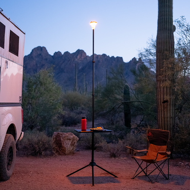 Black Outpost Table, 18"x24", clamped to a LightRanger pole with a red bottle and food, at dusk.