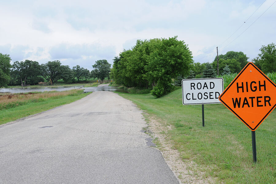Road closed and high-water warning signs in front of a flooded rural road