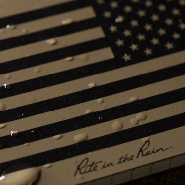 Tan and black American flag Rite in the Rain 3x5 top spiral notebook with water droplets.