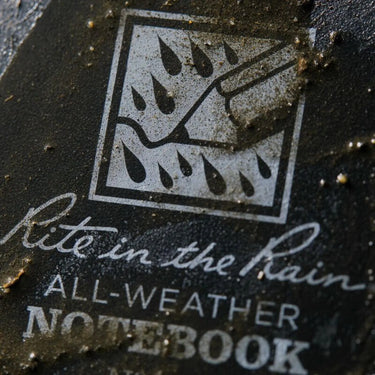 Close-up of a dirty black Rite in the Rain All-Weather Notebook cover with logo.