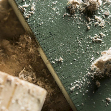 Close-up of a green Rite in the Rain soft cover book with a ruler pattern, covered in wood shavings.