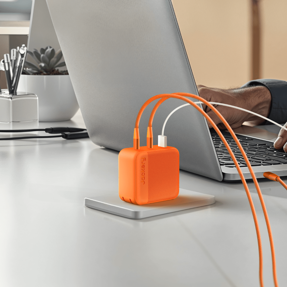 Orange Jackery 102W GaN 3-port fast charger with two USB-C cables plugged into a silver laptop.