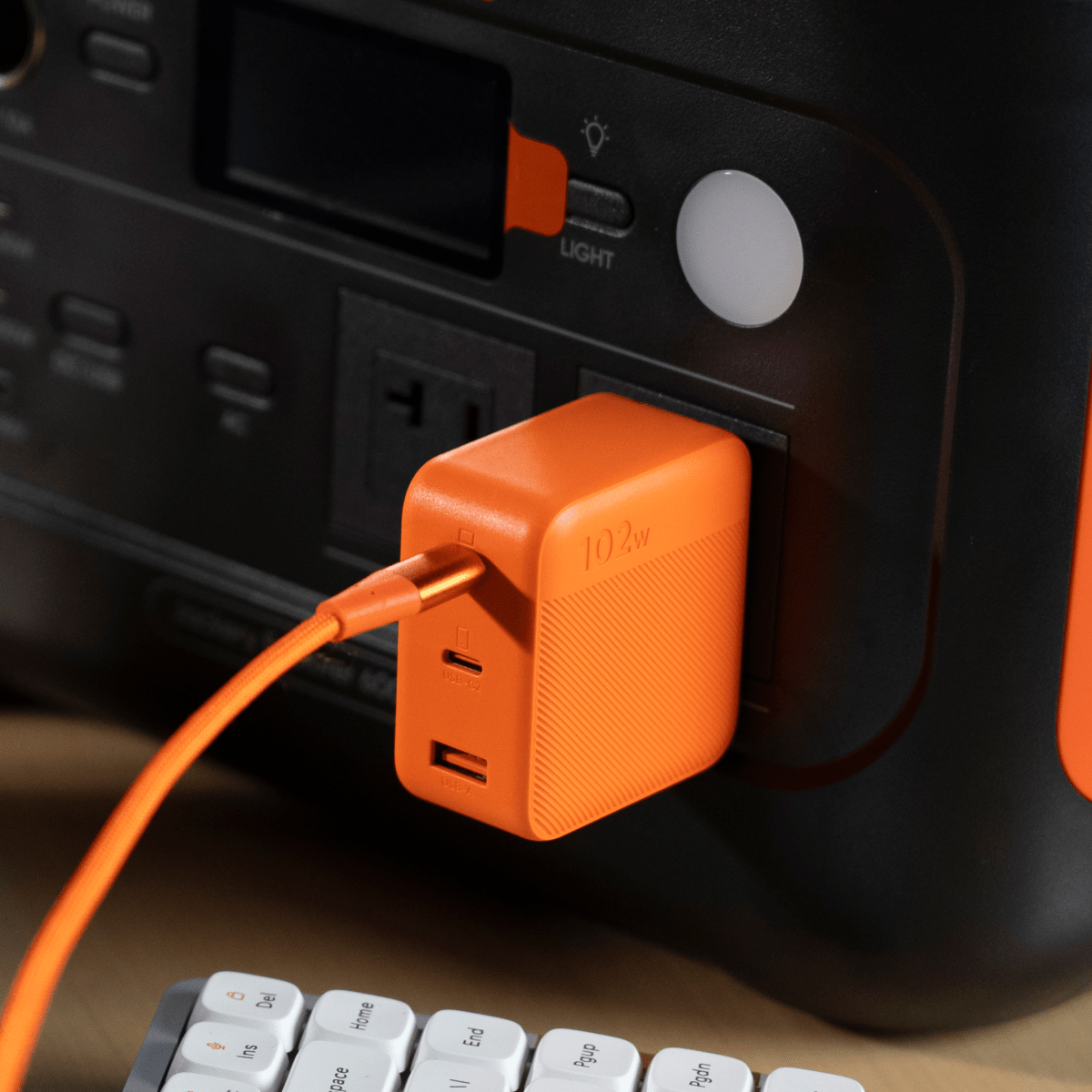 Orange Jackery 102W GaN 3-port fast charger plugged into a black power station, with an orange USB-C cable.
