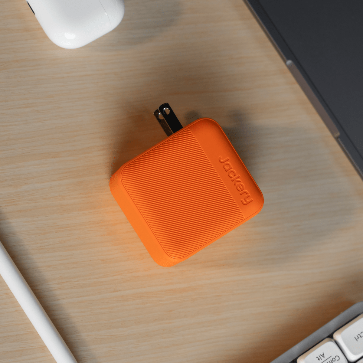 Orange Jackery 102W GaN 3-port fast charger with textured surface on a wooden desk.