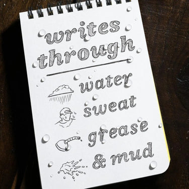 White spiral notebook with "writes through water, sweat, grease & mud" text and water droplets.