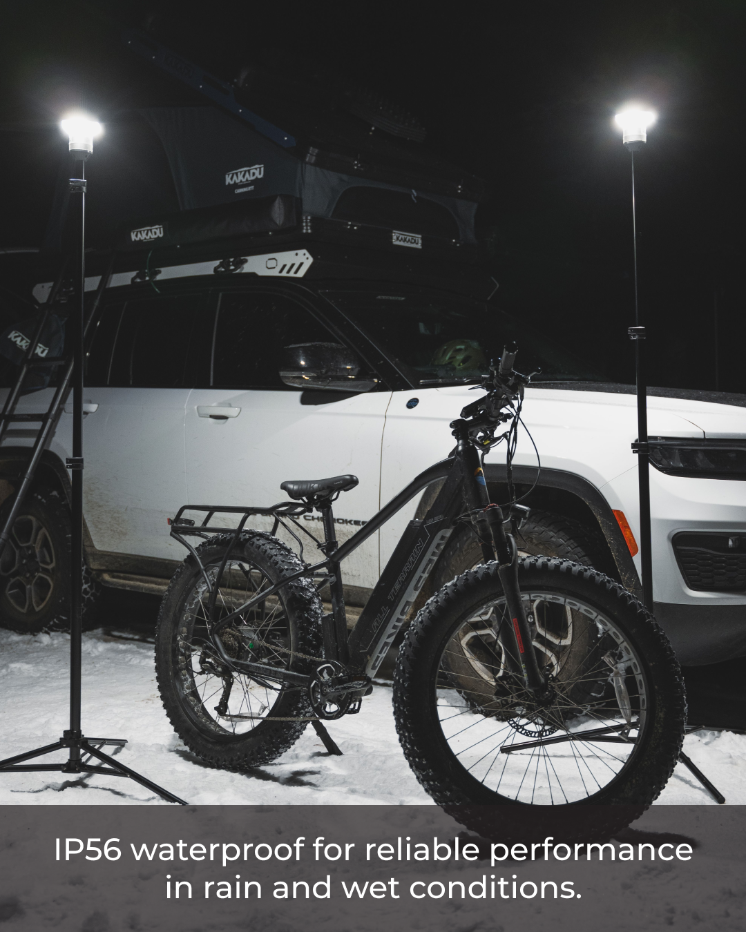Two bright Devos LightRanger 1200 lights illuminating a black fat-tire e-bike and white SUV with a rooftop tent at night.