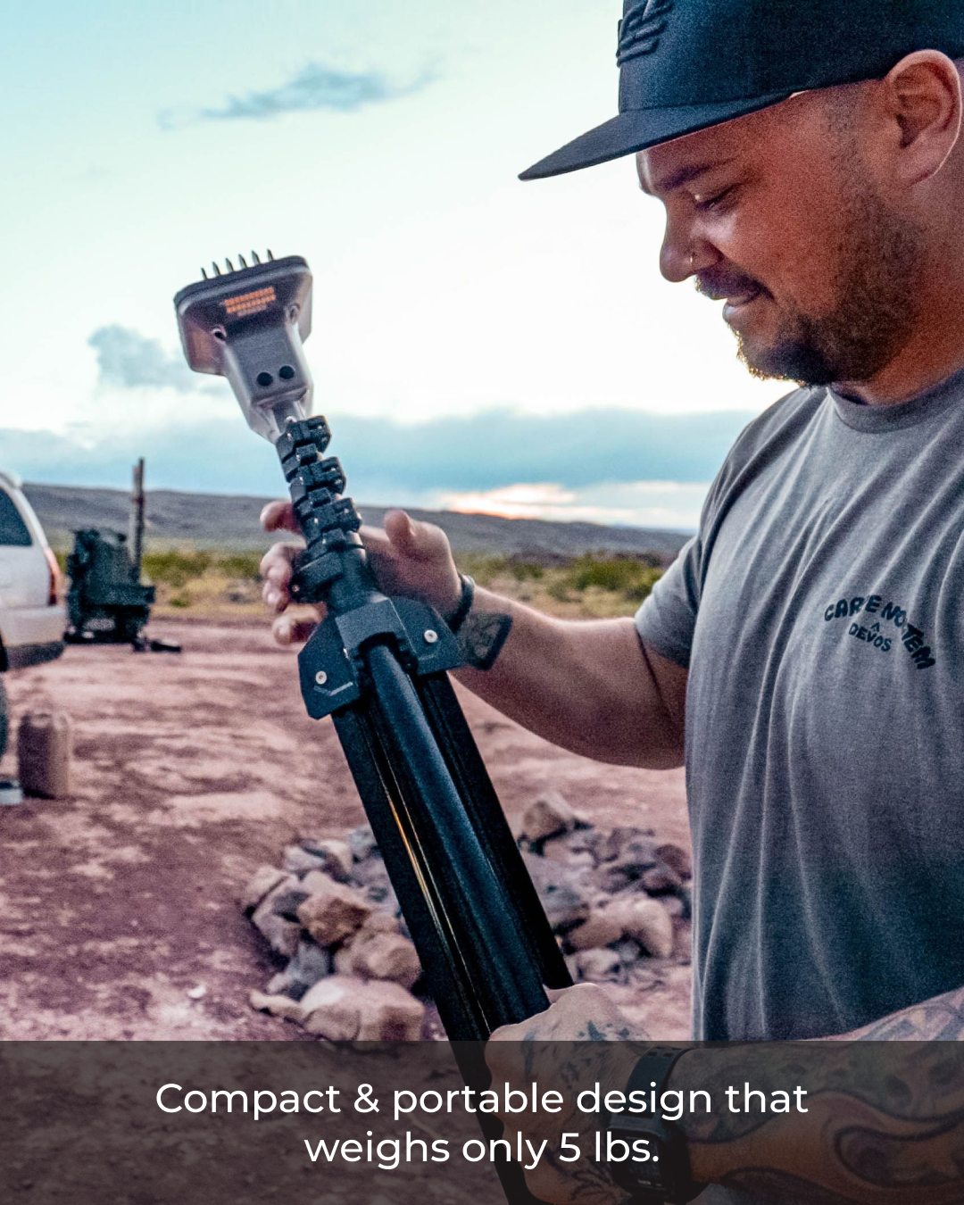 Man holding a compact black Devos LightRanger 2000, a telescoping outdoor lighting unit, in a desert setting.