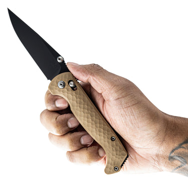 Hand holding a Dropwing folding knife with a coyote tan G10 handle and black CPM MagnaCut blade.