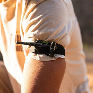 Black ETQ Gen 2 tourniquet with a green level, strapped to a person's upper arm over a tan shirt.