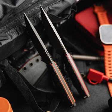Two black Toor Field 3.0 fixed blade knives with orange G10 liners, resting on a dark backpack.