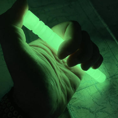 Hand holding a glowing green, ribbed Glo-Baton Kubaton over a map in the dark.