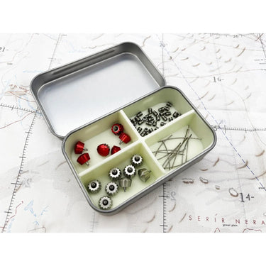 Open survival tin with a glow-in-the-dark silicone divider organizing small red and silver gear on a map.