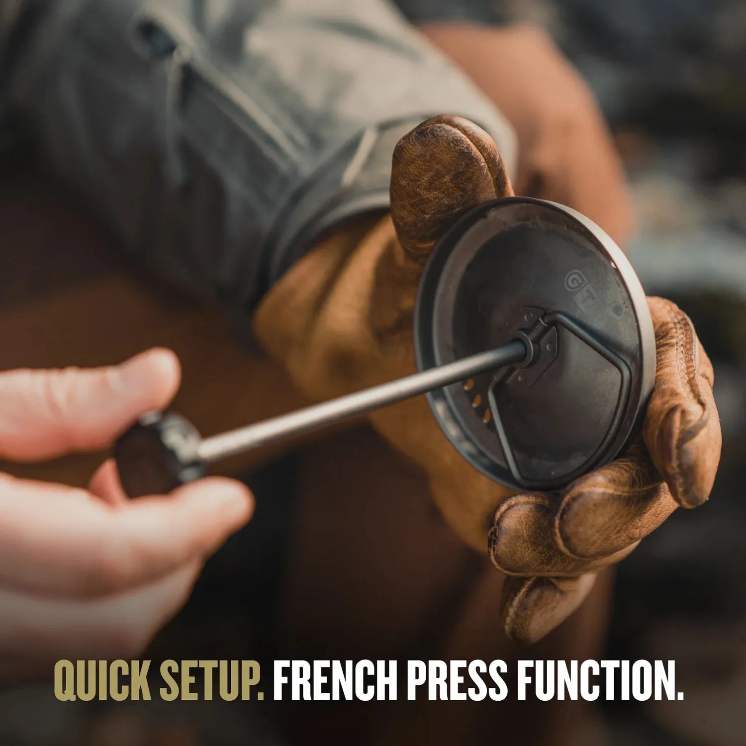 Hands in brown leather gloves assembling a dark gray titanium Grayl Coffee Press.