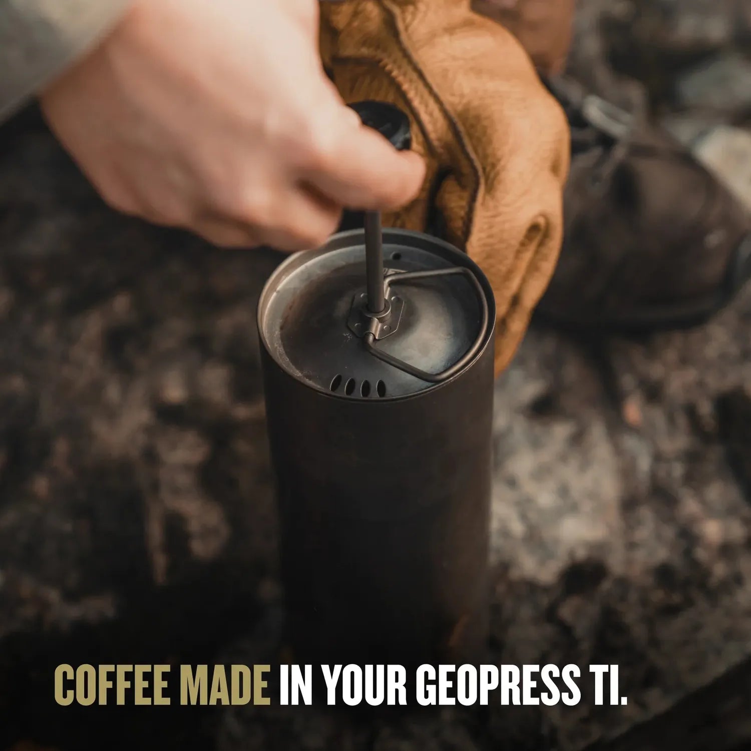 Hands in brown gloves pressing down the titanium Grayl Coffee Press inside a dark GeoPress Ti bottle.