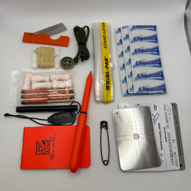 Collection of survival items including a knife, matches, and Aquatabs on a white background