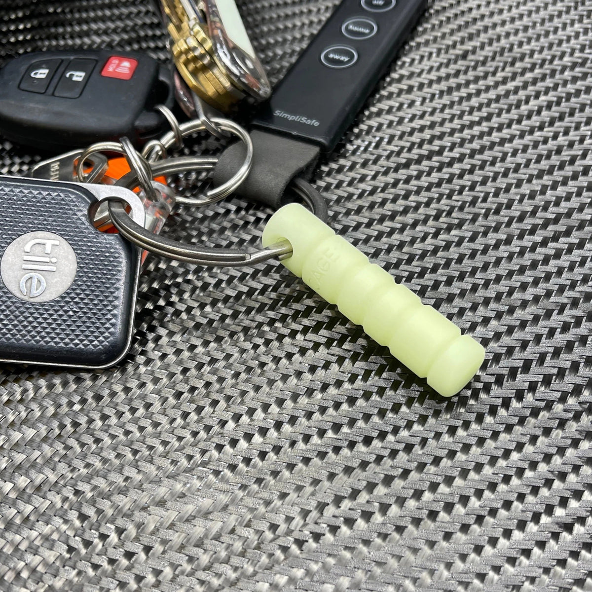 Keychain with a small device and a green glow stick on a textured surface