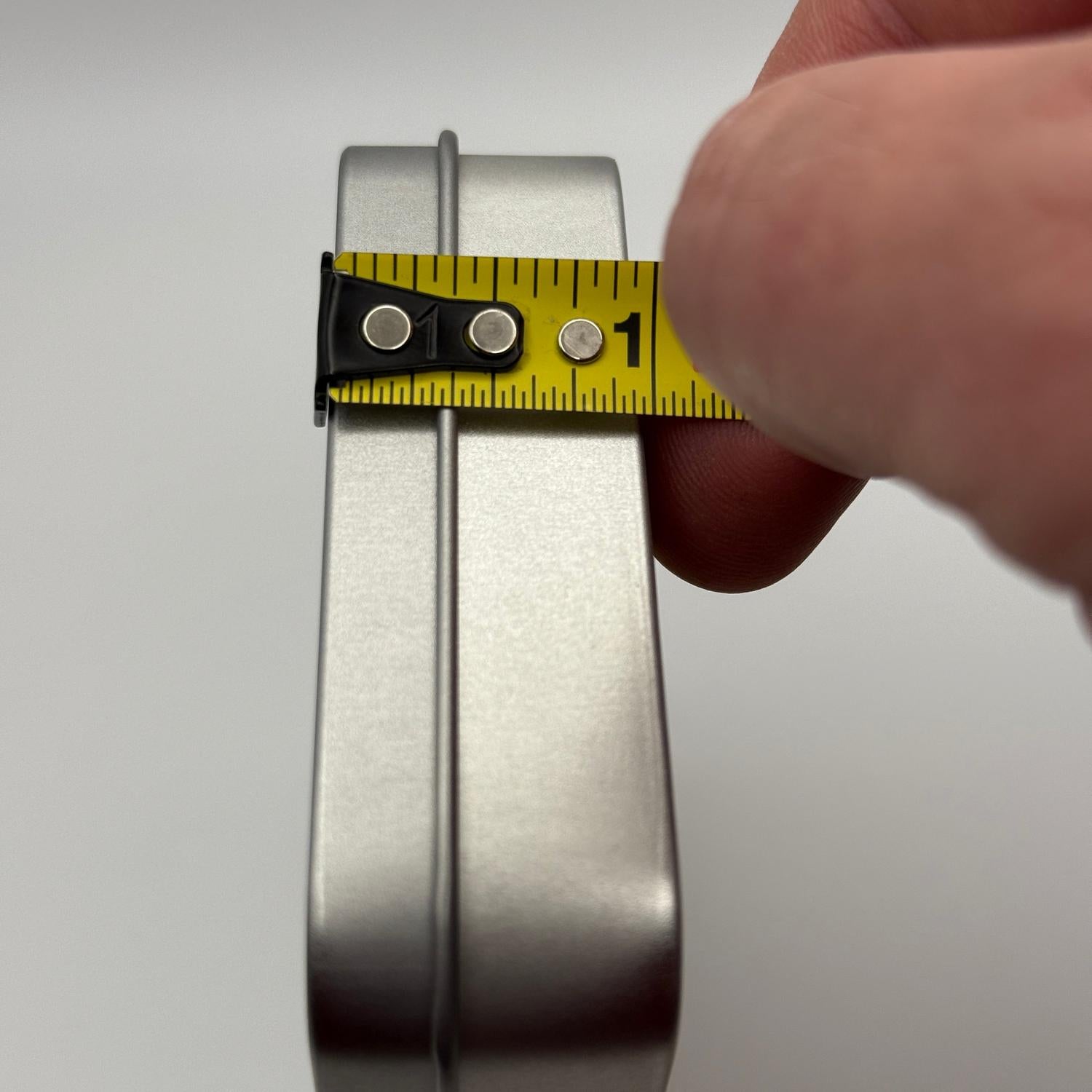 Hand holding a yellow tape measure against the narrow, silver, rectangular INCOG emergency sustainment kit.