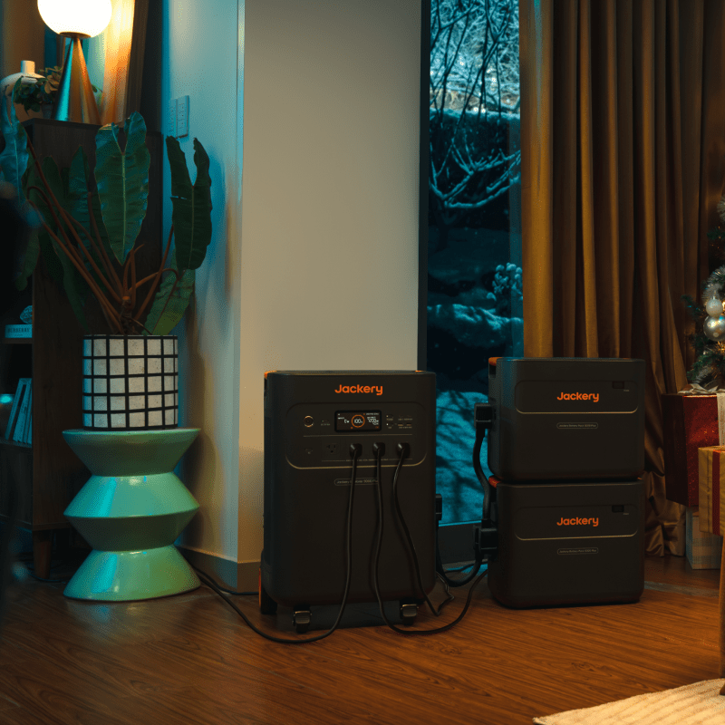 Jackery 5000 Plus battery pack and two stacked expansion batteries in a cozy indoor setting.