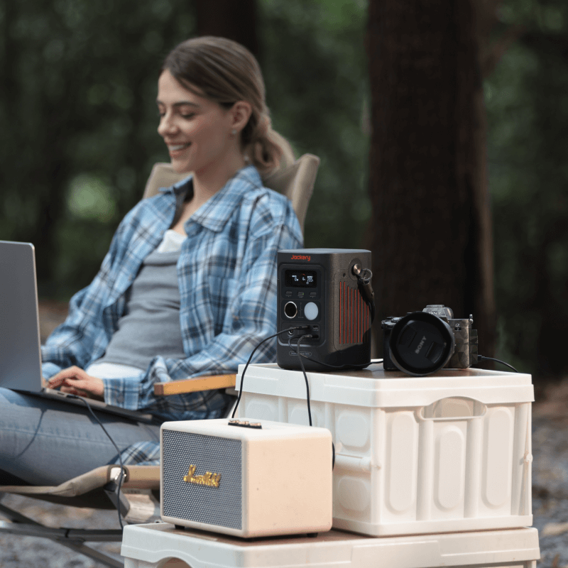 Jackery Explorer 300D portable power station, black with orange accents, charging devices outdoors.