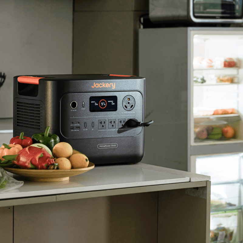 Jackery HomePower 3000 portable power station in dark gray with orange accents, plugged into a kitchen outlet.