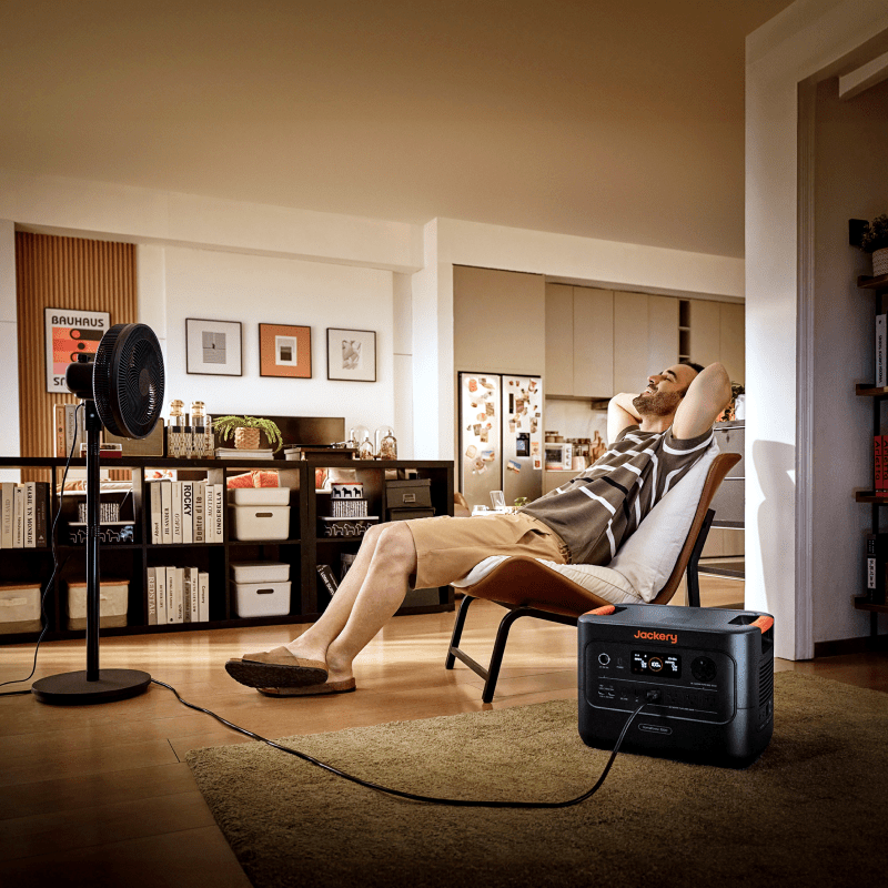 Jackery HomePower 3000, a compact black portable power station, powering a fan in a modern living room.