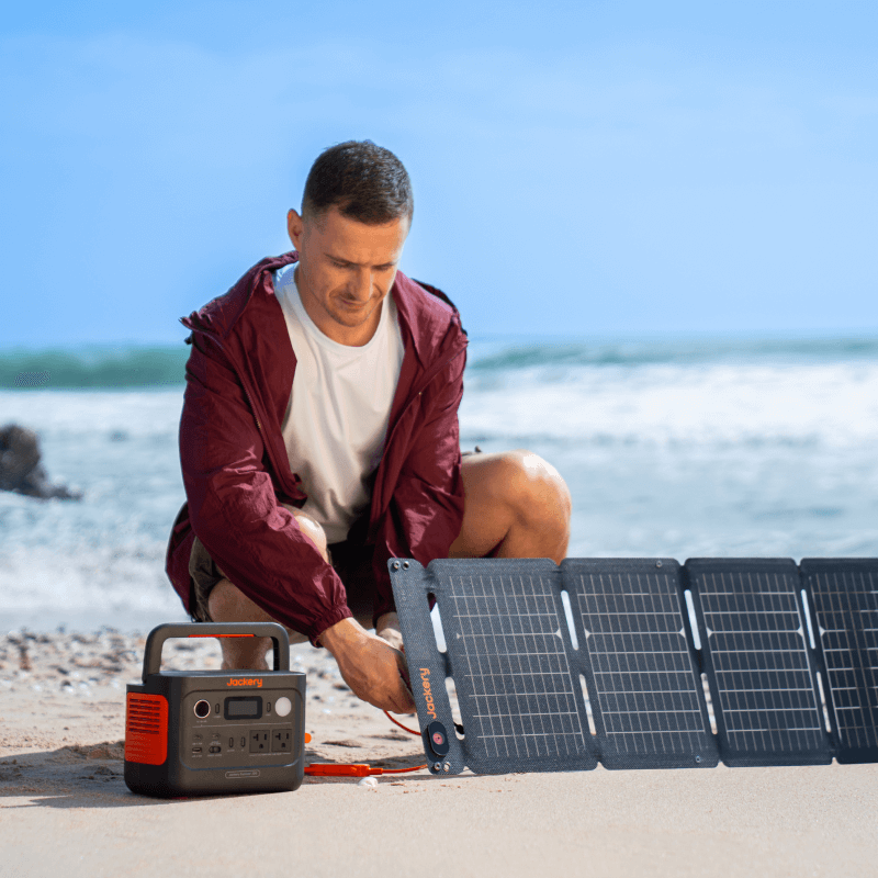 Man on a beach connecting a Jackery Explorer 300 v2 portable power station to a solar panel.