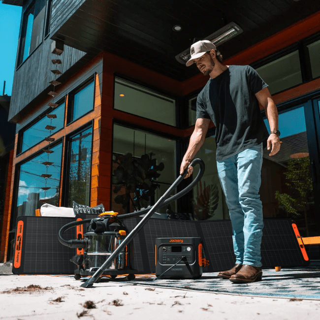 Man using a black Jackery Solar Generator 2000 v2 to power a shop vac outdoors.