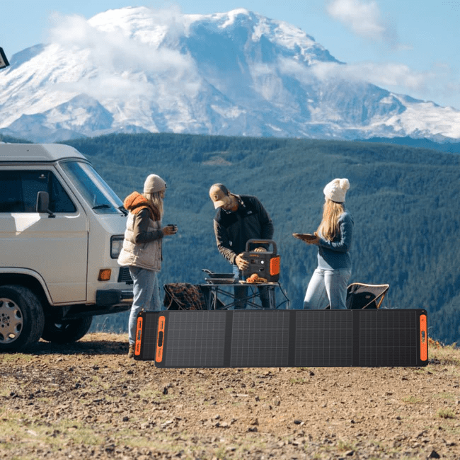Jackery Solar Generator 2000 v2 powering outdoor cooking with portable solar panels and a van, mountains in background.