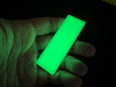 Hand holding a glowing green Maratac Find Me Glow Tag Patch, a 1x3 inch silicone gear identifier.