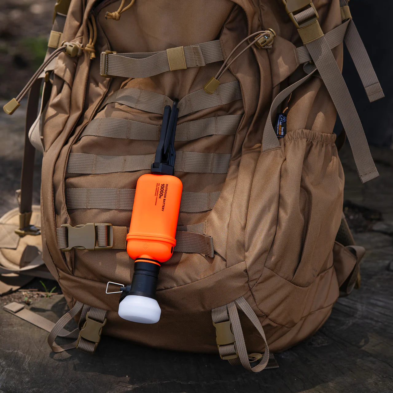 Orange NESTOUT 10,000mAh rugged power bank with black and white accents attached to a tan backpack.