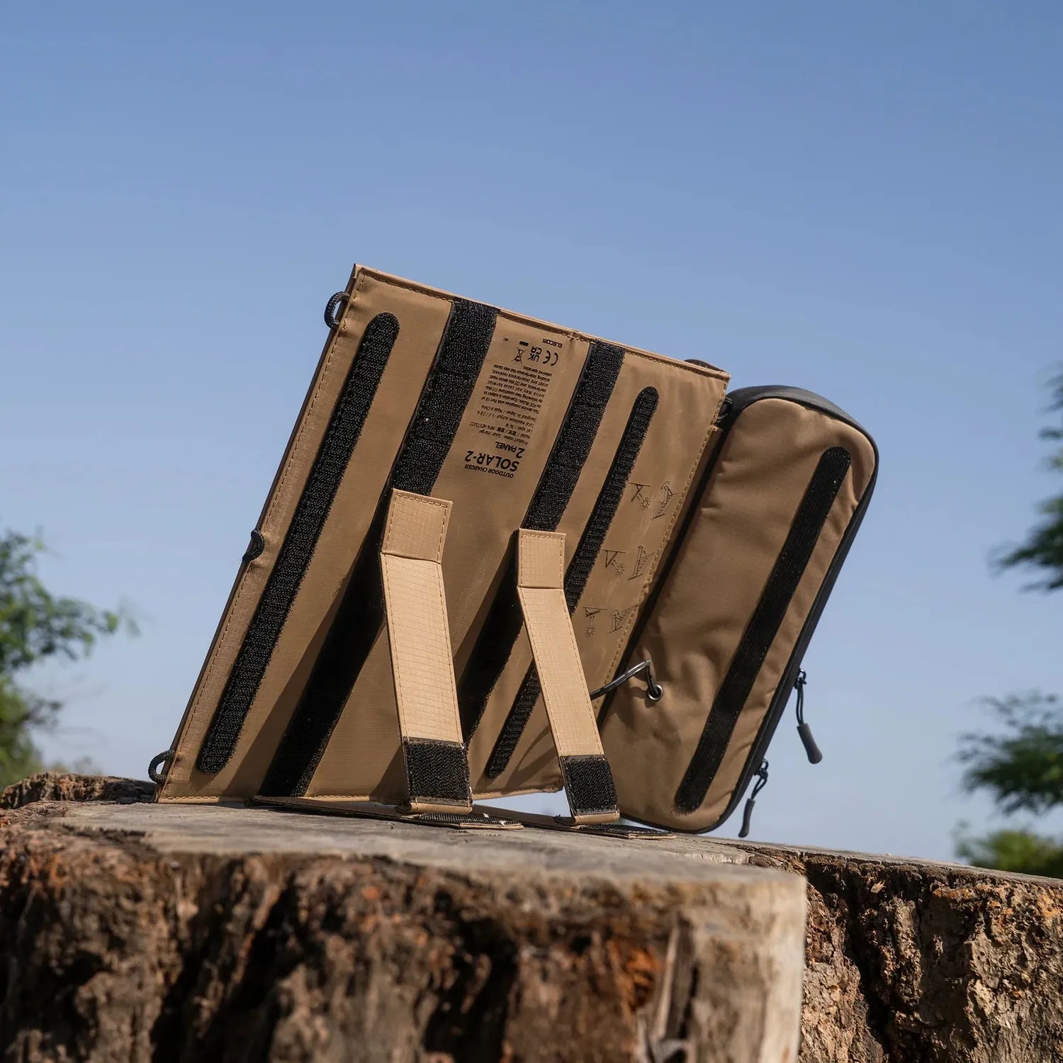 NESTOUT 2-Panel Solar Charger V2, tan and black, unfolded on a tree stump under a blue sky.