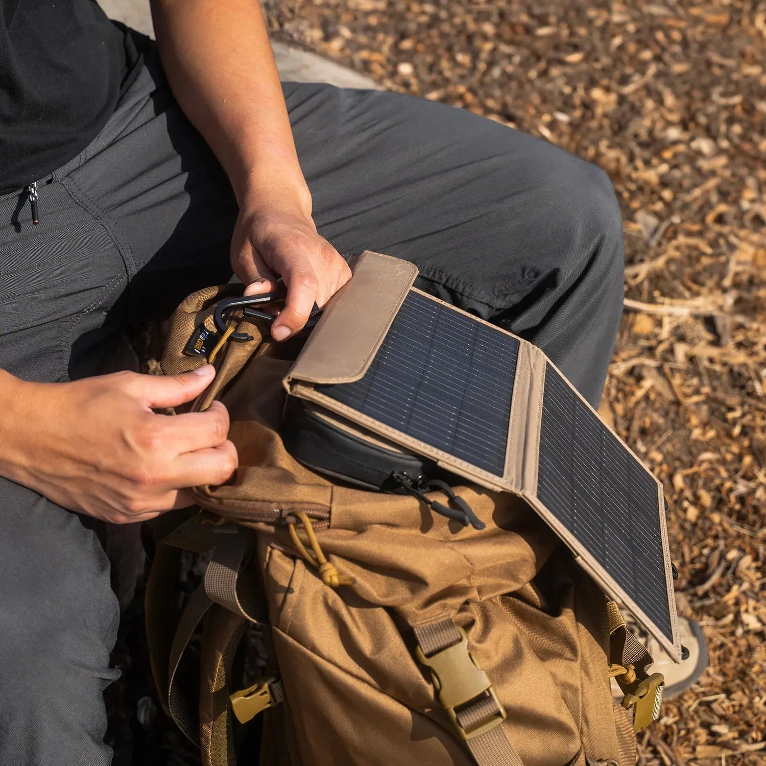 Person attaching a tan NESTOUT 2-panel solar charger with black monocrystalline cells to a brown backpack.