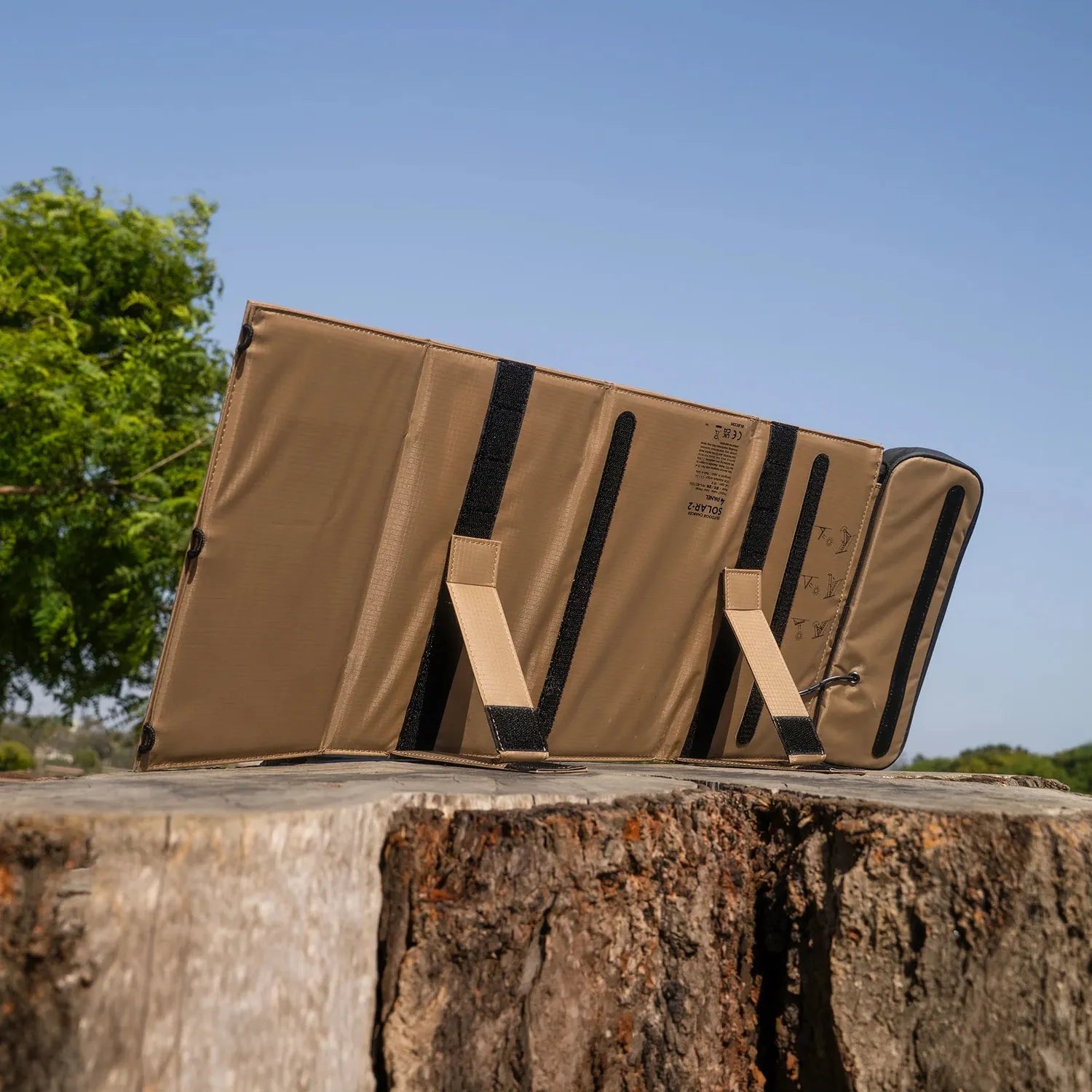 NESTOUT 4 Panel Solar Charger V2, tan fabric, unfolded on a tree stump outdoors.