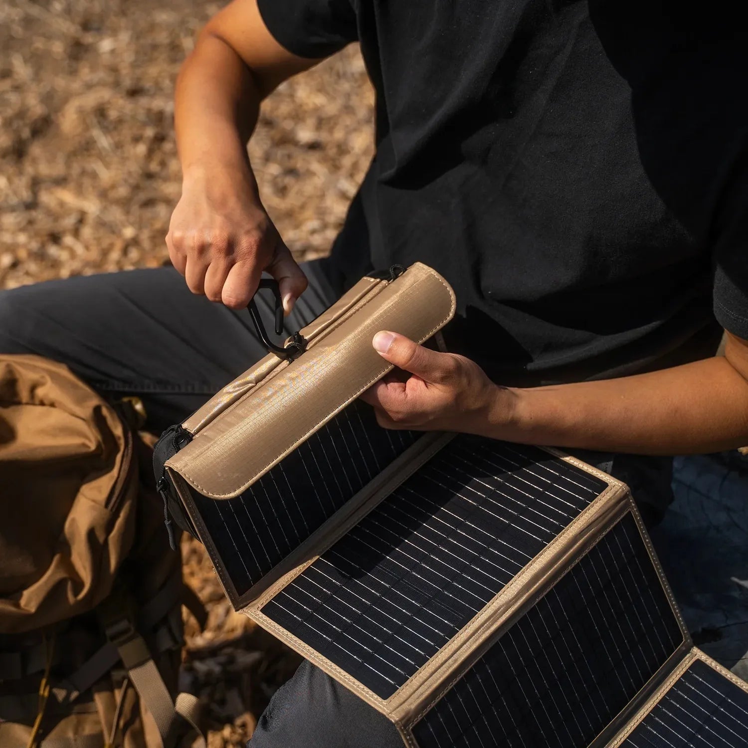 Person unfolding a tan NESTOUT 4-panel solar charger with black monocrystalline cells outdoors.