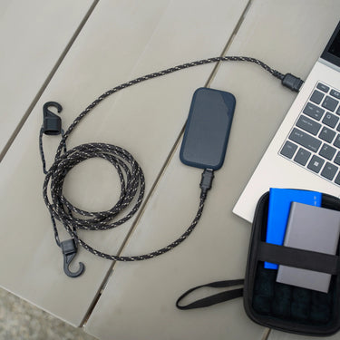 Rugged black and tan braided USB-A to USB-C outdoor charging cable with hooks, connected to a power bank and laptop.