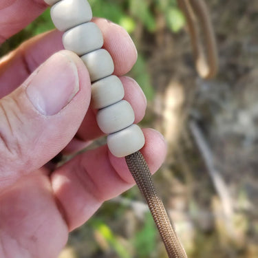 Hand holding tan pace count beads on a brown nylon cord, for land navigation.