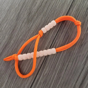 Hi-Viz orange paracord pace counter with 13 phosphorescent glow-in-the-dark beads on a wooden surface.