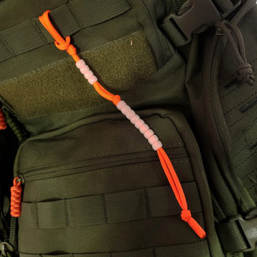Orange cord phosphorescent pace counter beads on an olive green backpack.
