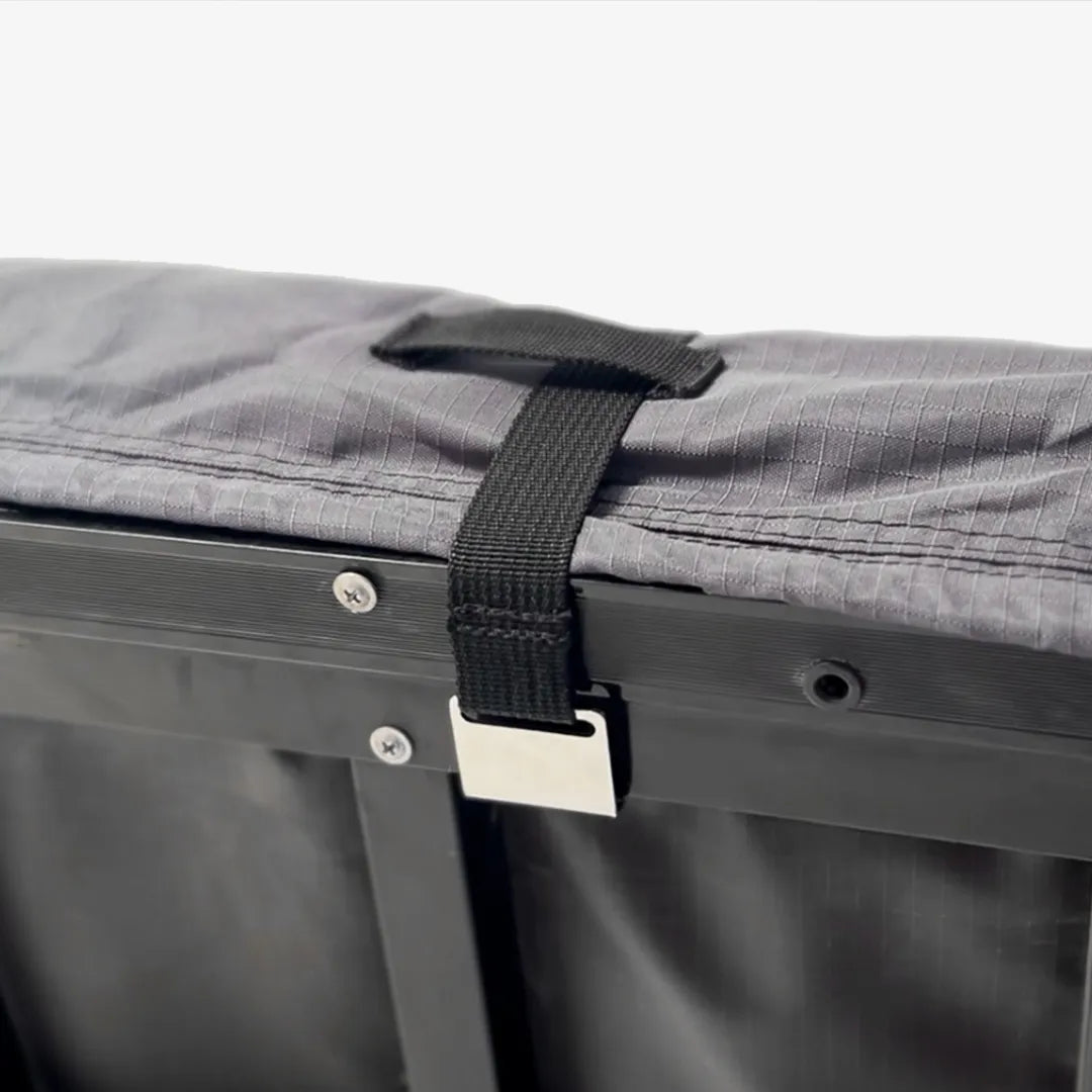 Gray protective cover for a rooftop tent, secured by a black strap with a silver buckle.