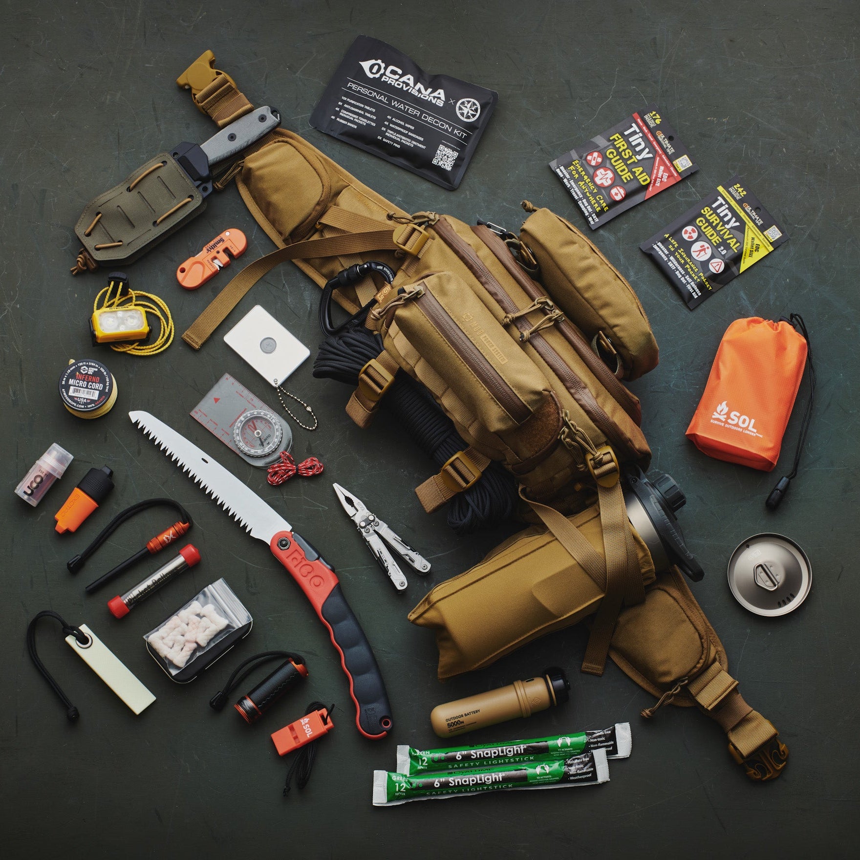 Assorted survival gear including a tactical hip pack, tools, and supplies on a dark surface.