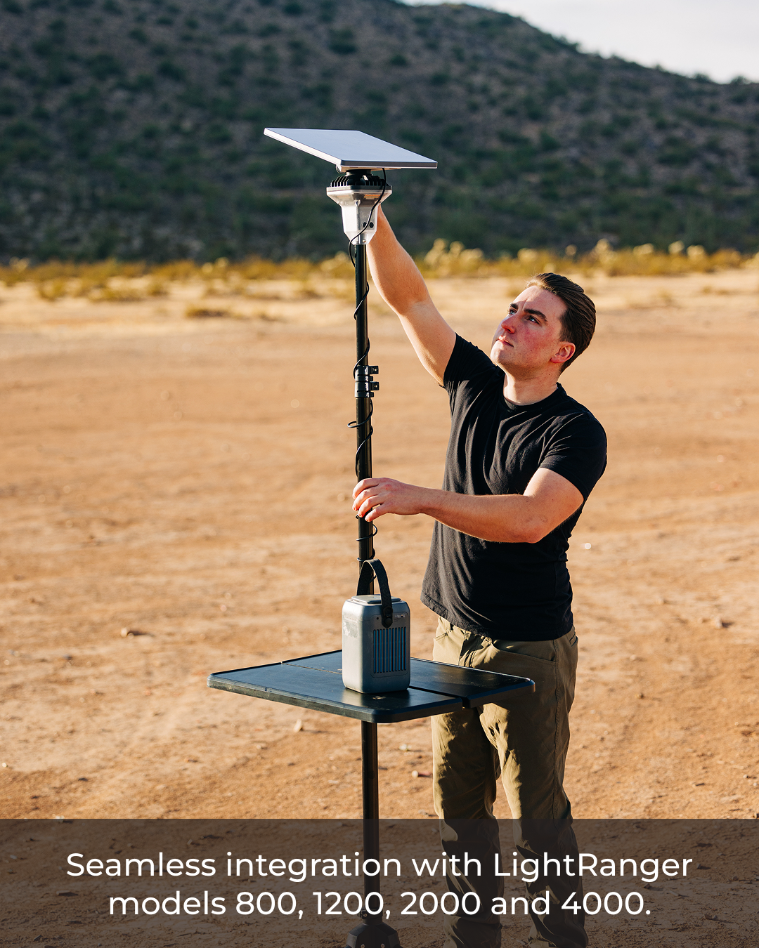 Man adjusting a black Starlink Mini Mount with a Starlink dish on a LightRanger pole in a desert landscape.