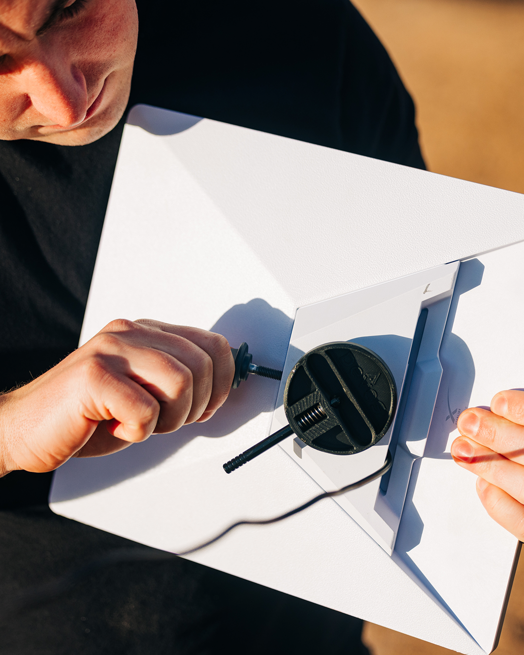 Person's hands attaching a black Starlink Mini pipe adapter to a white rectangular mount.