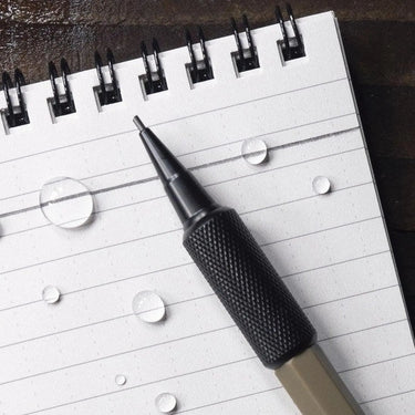 Flat Dark Earth mechanical pencil with a black knurled grip on a wet, lined notepad.