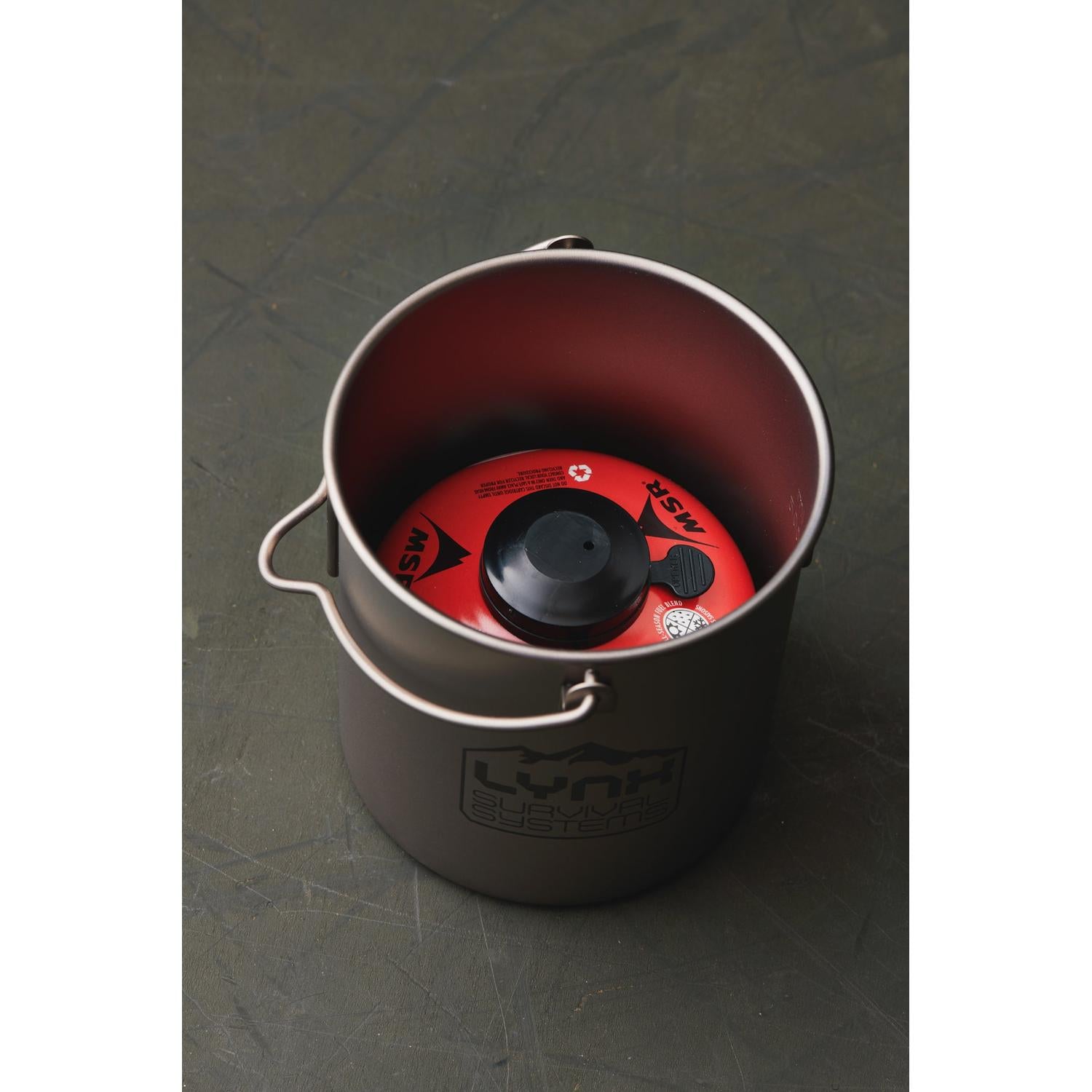 Gray titanium 750ml ultralight pot with "LYNX Survival Systems" logo, holding a red MSR fuel canister.