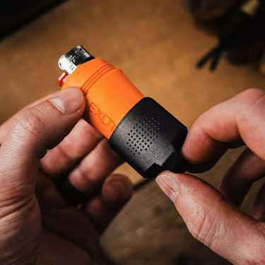 Hands hold an orange and black Exotac fireSLEEVE Mini waterproof lighter case with a mini BIC lighter inside.