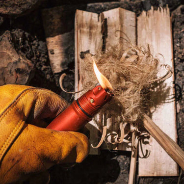 Hand holding an orange lighter with a wooden stick against a stone wall background